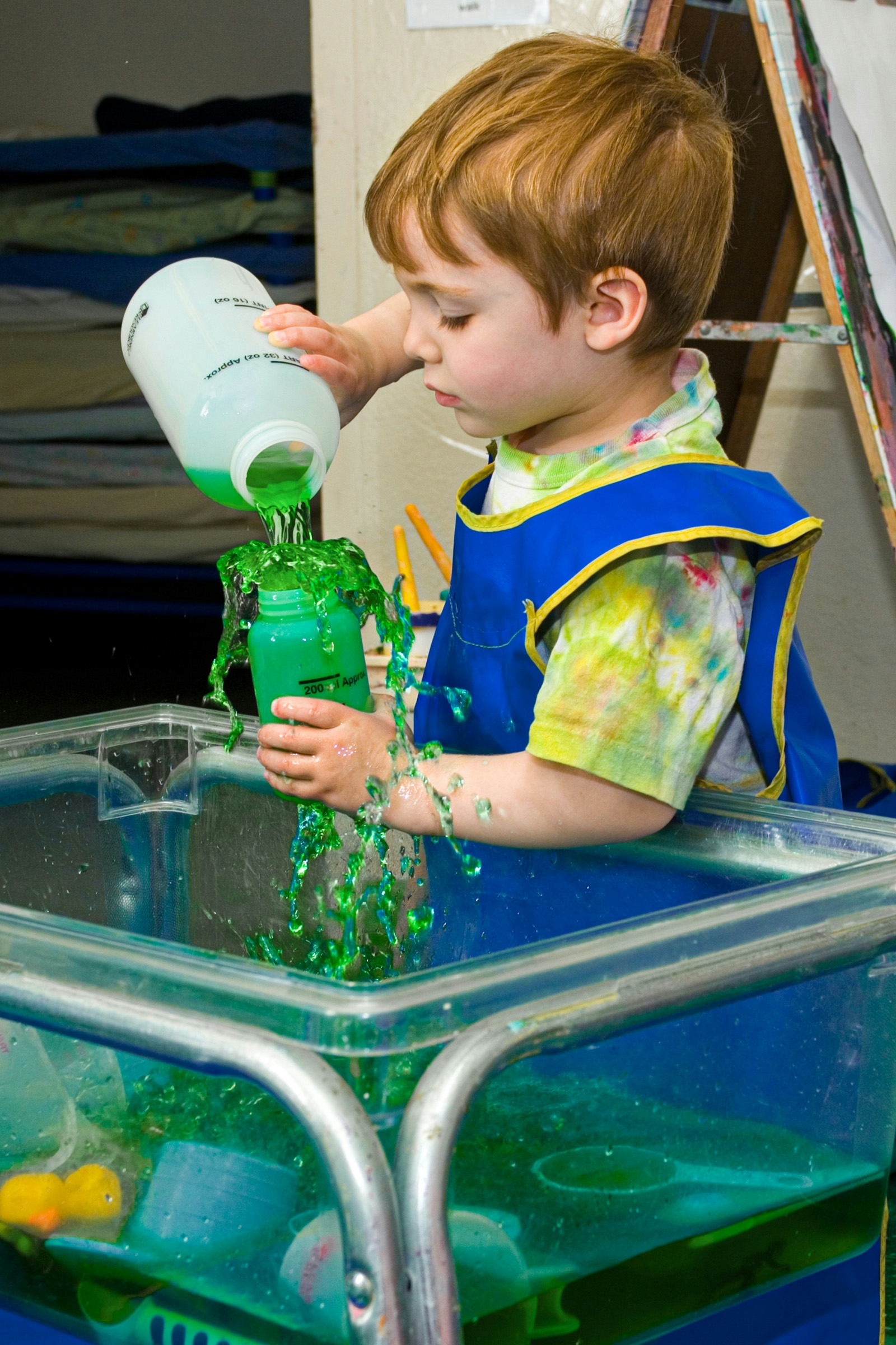 Boy (3) splashes colored water while playing at water table