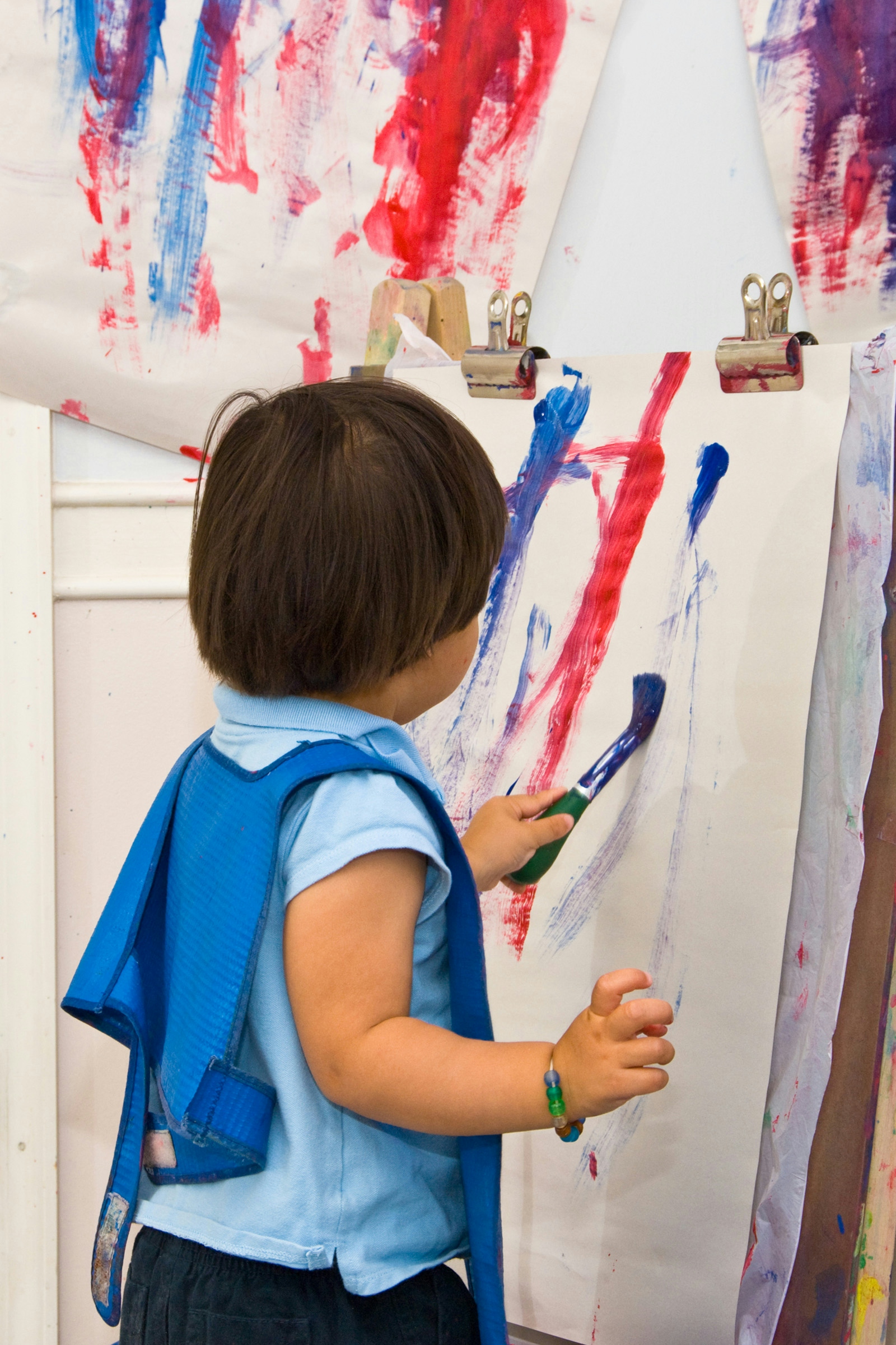 Toddler (age 2) paints with red and blue paint at daycare