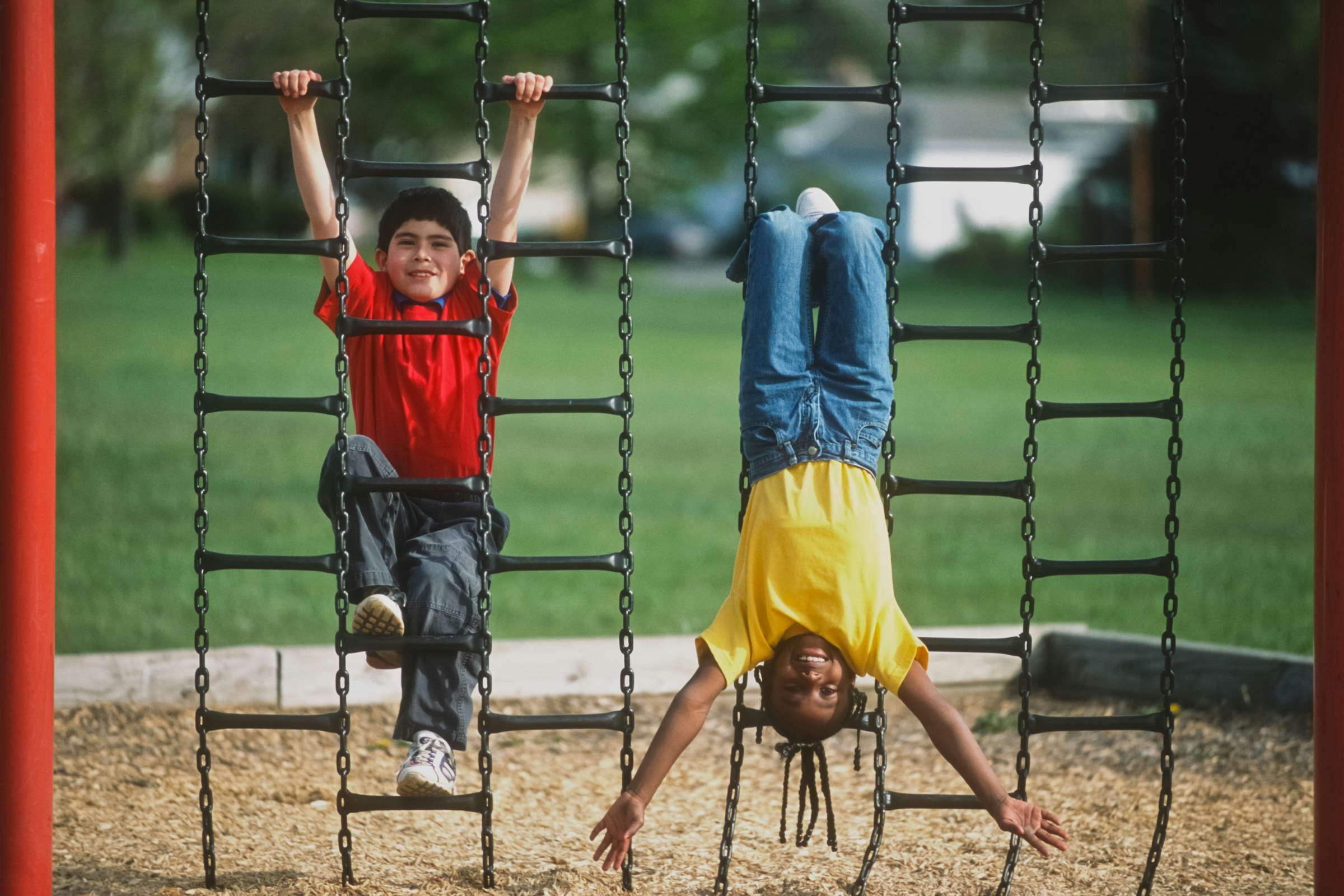 Girl and boy play on hanging structure on playground